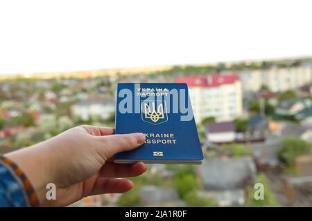 Recentrer le passeport d'un citoyen ukrainien dans une main féminine sur un fond urbain flou, gros plan. Inscription au passeport ukrainien. Guerre. Par Banque D'Images