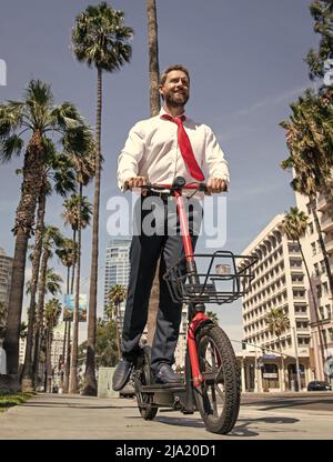 Un avocat heureux en tenue de formalwear se déplace e-scooter sur le trottoir, à cheval Banque D'Images