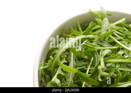 Feuilles d'arugula ou de rucola vertes fraîches dans un bol blanc isolé sur un fond blanc. Vue de dessus sur Eruca vesicaria, une plante utilisée comme un légume de salade. Banque D'Images