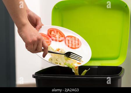 Gros plan d'une personne qui jette une banane à moitié finie avec des légumes dans la poubelle.concept de déchets alimentaires qui est en bon état Banque D'Images