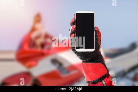 Smartphone Biker portable avec écran vierge, image rognée, espace de copie, écran vide pour le design graphique avec une moto en arrière-plan Banque D'Images