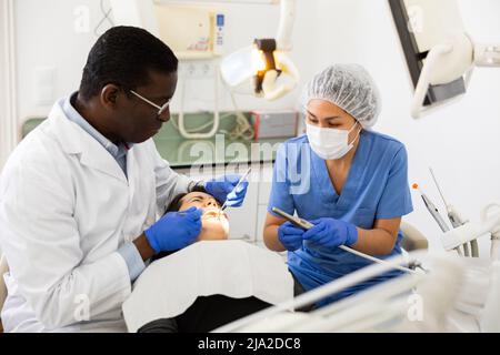 Stomatologue ciblé avec une assistante féminine traitant les dents d'une patiente Banque D'Images