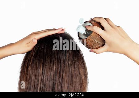 Femme appliquant la bouteille d'huile de noix de coco et le chapeau aux cheveux dans une main sur blanc isoler vue arrière Banque D'Images