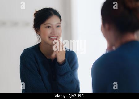 Portrait de la jeune femme asiatique regardant dans le miroir vérifiant son visage à la salle de bains. Concept de style de vie. Banque D'Images