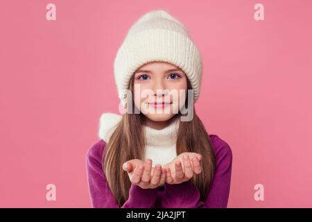 Portrait mignon petite fille en tricoté chaud couleur gris chapeau, écharpe et mitaines envoi soufflant un air de baiser sur fond rose en studio.enfants hiver Banque D'Images