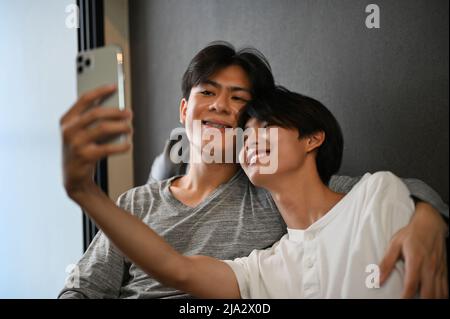Asiatique adolescent gay couple prenant un selfie ensemble dans la salle de séjour, main de partenaire est autour de son amant, montrant une certaine affection LGBT. Concept LGBT Banque D'Images