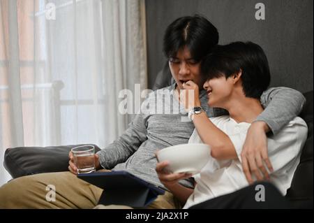 Un beau couple asiatique adolescent gay se détend dans le salon ensemble, un homme nourrissant un en-cas à son ami gay. GGBT gay dans l'amour concept. Banque D'Images
