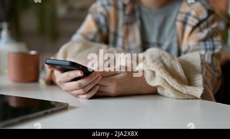 Une femme indépendante s'assoit à son bureau et utilise son smartphone. Photo courte, gros plan Banque D'Images
