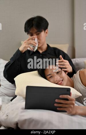 Un beau couple asiatique de jeunes hommes gay se détend dans la chambre, regardant le film sur une tablette ensemble. Un homme allongé sur l'oreiller sur son petit ami genoux. Romanti Banque D'Images