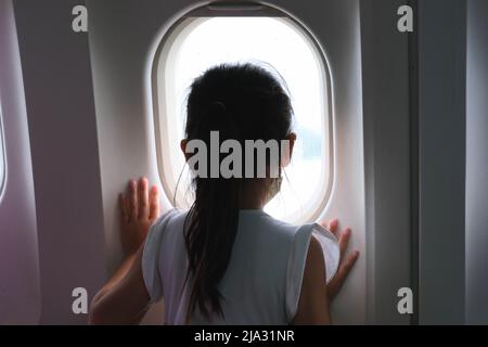 Petite fille mignonne voyageant à bord d'un avion. Enfant fille regardant la vue aérienne du ciel et nuage à l'extérieur de la fenêtre d'avion tout en étant assis sur le siège d'avion. tra Banque D'Images