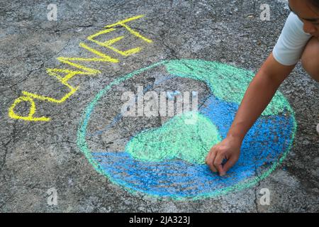 Jeune femme dessin avec de la craie colorée sur l'asphalte. Femme asiatique peint un monde magnifique avec le message planète sur cour. Concept de l'envir du monde Banque D'Images