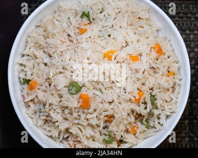 Vue de dessus du riz frit aux légumes dans un bol en céramique blanc sur fond de tapis de table. Banque D'Images