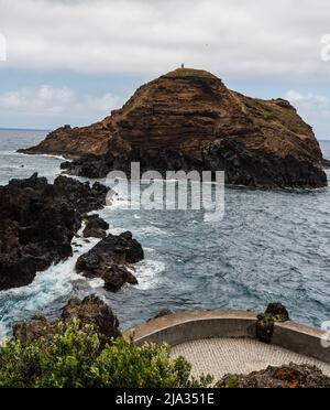 Petite île rocheuse avec phare près de Porto Moniz à Madère pendant une journée très nuageux Banque D'Images