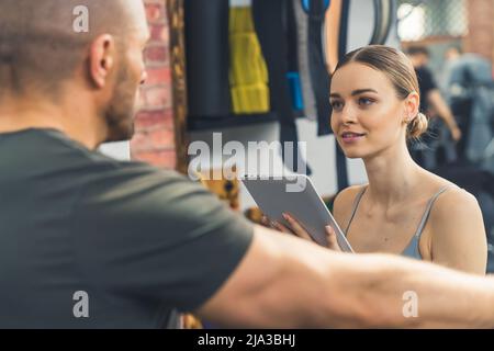 Belle femme caucasienne écrit un plan d'entraînement avec un entraîneur à la salle de gym. Photo de haute qualité Banque D'Images