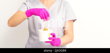 Portrait d'une esthéticienne caucasienne tenant un pot de pâte de sucre pour sugarer portant des gants roses sur fond blanc Banque D'Images