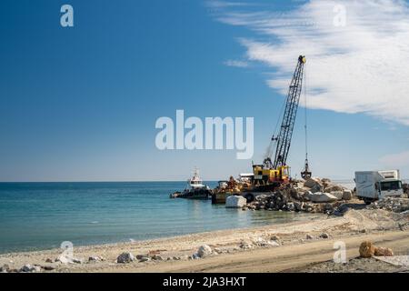 Une grue hydraulique de manutention de roches se déplaçant et plaçant des roches sur le rivage Banque D'Images