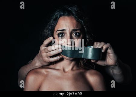 Femme mise au silence par son partenaire. Les mains de l'homme mettant sur le ruban adhésif de conduit sur sa bouche Banque D'Images