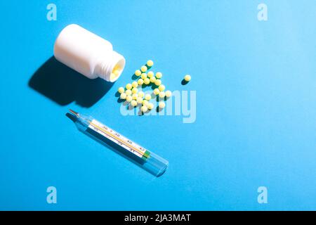 Pilules à bille jaunes et thermomètre sur fond bleu. Concept minimal de médecine plat. Banque D'Images