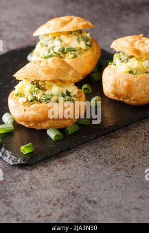 Des profiteroles farcies de salade d'oeufs avec des oignons verts sur un tableau d'ardoise sur la table. Vertical Banque D'Images