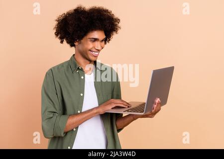 Portrait de l'attrayant gai qualifié à cheveux ondulés en utilisant l'ordinateur portable dactylographiant e-mail isolé sur fond beige pastel couleur Banque D'Images