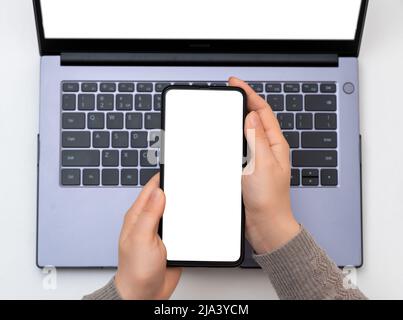 mains d'une femme avec téléphone cellulaire sur fond de clavier d'ordinateur portable. Vue de dessus maquette de mains tenant un écran blanc vierge téléphone mobile avec ordinateur portable Banque D'Images