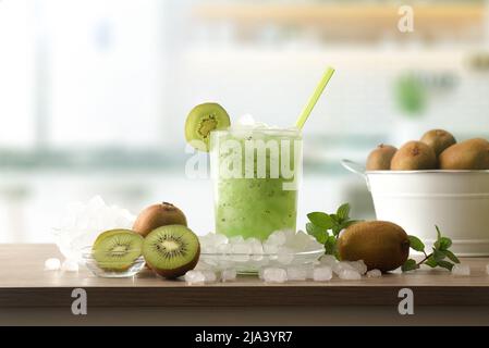 Détail de la boisson sans alcool kiwi avec beaucoup de glace sur un banc de cuisine en bois avec des fruits et un bol avec de la glace autour d'elle. Vue avant. Composition horizontale. Banque D'Images