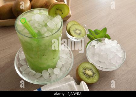 Détail de la boisson sans alcool kiwi avec beaucoup de glace sur un banc de cuisine en bois avec des fruits et un bol avec de la glace autour d'elle. Vue en hauteur du dessus. Position horizontale Banque D'Images