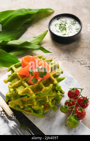 Gaufres belges vertes. Épinards ou ail sauvage ou gaufres au pesto avec saumon rouge et sauce à la crème sur fond de table en béton gris. Délicieux petit déjeuner, Banque D'Images