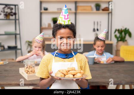 Cute little boy tamisant la farine sur bol en allant faire de la pâte de pâtisserie maison dans la cuisine Banque D'Images
