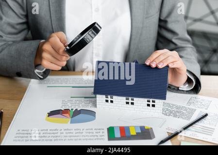 vue rognée de l'inspecteur des impôts tenant la loupe au-dessus du modèle de maison près des cartes sur la table Banque D'Images