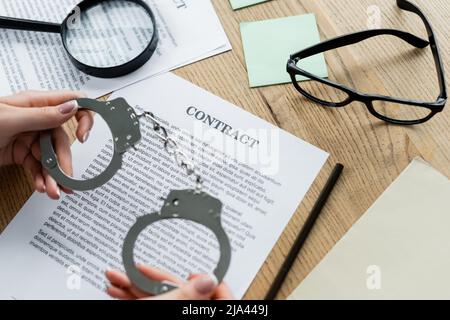 vue rognée de l'inspecteur des impôts tenant les menottes près de la loupe et les documents sur le bureau Banque D'Images