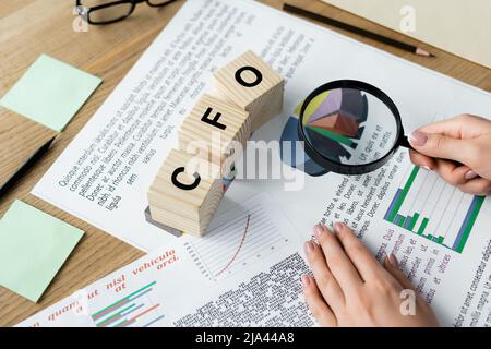 vue rognée de la femme tenant la loupe au-dessus des tableaux près des cubes avec le lettrage cfo sur le bureau Banque D'Images