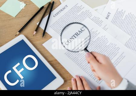 vue rognée d'une femme tenant une loupe près du contrat et d'une tablette numérique avec lettrage cfo Banque D'Images
