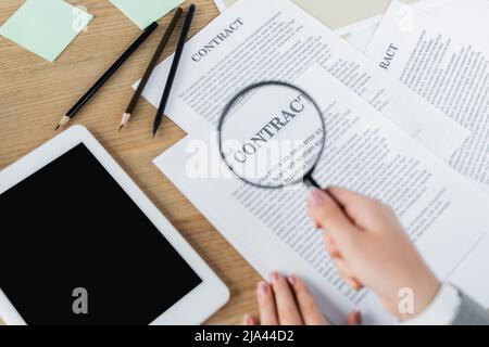 vue rognée de la femme tenant la loupe près du contrat et de la tablette numérique avec écran vide Banque D'Images