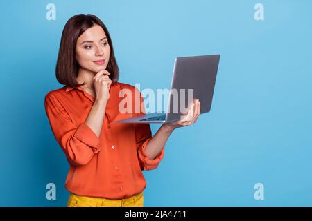 Portrait d'une jolie jeune fille douée et orientée à l'aide d'un ordinateur portable qui pense isolé sur fond bleu vif Banque D'Images