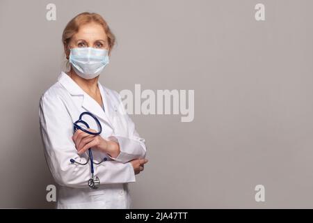 Femme médecin portant un uniforme et un masque médical de protection sur fond gris Banque D'Images