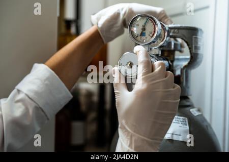 Gros plan des mains d'un technicien en gants pour régler un baromètre d'une bouteille d'azote ou d'air comprimé Banque D'Images