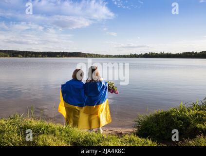 Les enfants se tiennent avec leur dos sur la rive d'un lac avec un drapeau ukrainien bleu-jaune. Famille, réfugiés, unité, soutien. Les Ukrainiens sont contre Banque D'Images