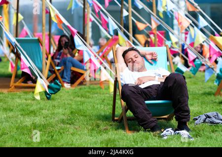 Hay Festival, Hay on Wye, pays de Galles, Royaume-Uni – vendredi 27th mai 2022 – Un visiteur profite de la possibilité de s'asseoir et de se reposer au soleil sur les pelouses du Festival entre les événements du deuxième jour de cette année Hay Festival – c'est la première fois que l'événement se tient en personne depuis 2019. Le Hay Festival se déroule jusqu'au 5th juin 2022. Photo Steven May / Alamy Live News Banque D'Images