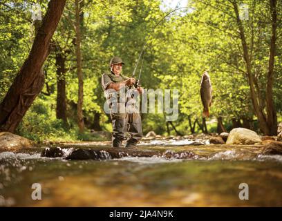 Pêcheur tirant un poisson de carpe hors d'une rivière dans les bois Banque D'Images