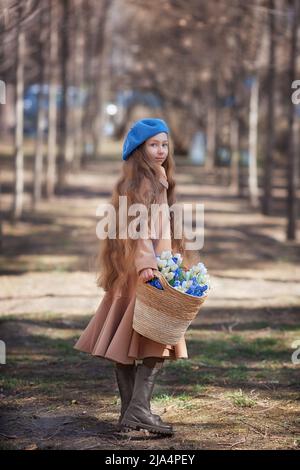 Petite jolie petite fille qui marche à travers la forêt au printemps et recueille les premières fleurs dans le panier . Banque D'Images