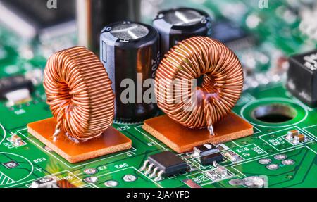 Gros plan d'inductances toroïdales et de condensateurs électrolytiques sur circuit imprimé vert électronique avec bokeh. Deux bobines de noyau en ferrite avec enroulement de fil en cuivre. Banque D'Images