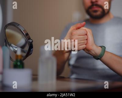 Concept de beauté pour hommes. Un homme de race blanche qui vérifie sa peau. Un homme à la barbe tire la crème de soin de la peau, les mains des hommes utilisant la crème hydratante, la peau et les soins des mains. Banque D'Images