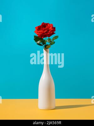 Concept romantique avec bouteille de champagne blanc et fleur de rose rouge. Arrière-plan élégant et minimaliste. Banque D'Images