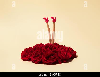 Les jambes d'une femme en chaussures roses émergent d'une pile de roses rouges. Composition créative minimale. Concept romantique. Banque D'Images