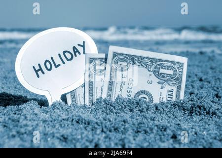 Billets de papier un dollar et un petit bâton avec la bulle de la parole de papier avec le mot vacances enterrées dans le fond de plage de sable mer, jour ensoleillé d'été. Concept argent voyage tourisme vacances détente. Couleur bleue Banque D'Images