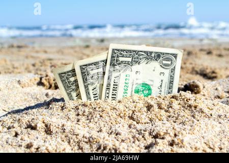 Trois billets en papier d'un dollar à moitié ensevelis dans le sable sur le bord de mer gros plan. Concept argent, affaires, épargne, financier, investissement, espèces. Banque D'Images