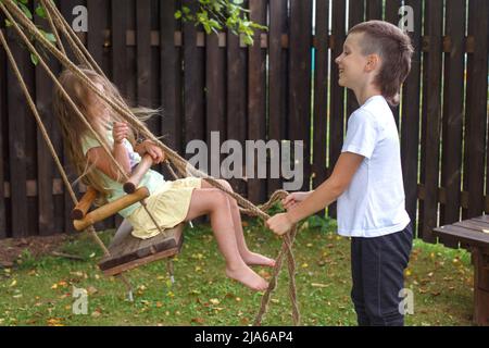 Un petit garçon et une fille se balancent dans le village. Frère joue avec sa sœur. Banque D'Images