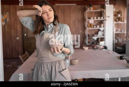 potter, jeune artisan fatigué, s'est concentré sur la sculpture d'un bol d'argile crue, le temps d'une leçon de poterie ou d'un atelier, une femme dans un studio créatif Banque D'Images