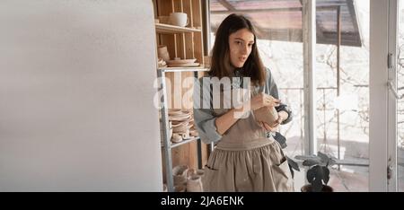 Un jeune artisan s'est concentré sur la sculpture d'une carafe d'argile brute lors d'un cours de poterie ou d'un atelier dans un studio créatif. Un jeune céramiste est engagé dans Banque D'Images